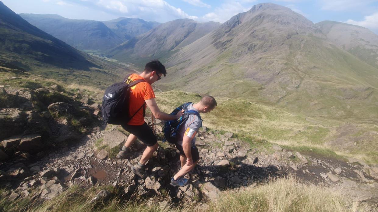 Blind man holds onto his friend's rucksack as they climb down a mountain peak