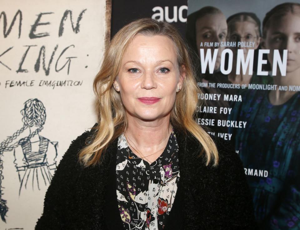 samantha mathis wearing a black shit and multi colored scarf, smiling and standing in front of the movie poster for the film women talking