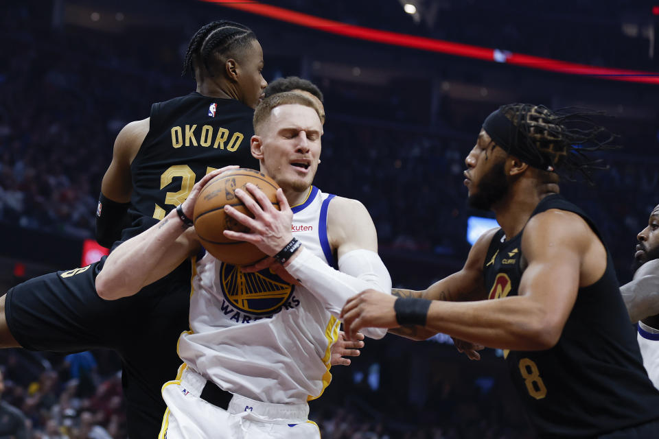 Golden State Warriors guard Donte DiVincenzo, center, grabs a rebound next to Cleveland Cavaliers' Lamar Stevens, right, and Isaac Okoro during the first half of an NBA basketball game Friday, Jan. 20, 2023, in Cleveland. (AP Photo/Ron Schwane)