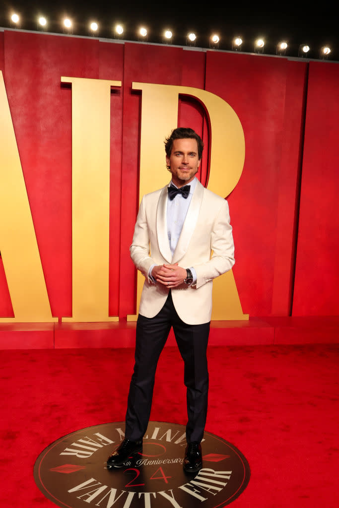 Man in a white jacket and bow tie standing in front of large 'Vanity Fair' letters