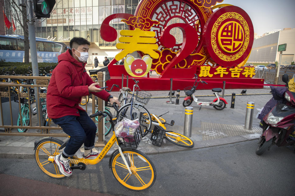 In this Jan. 22, 2020 file photo, a man wears a face mask as rides a bicycle past a display for the upcoming Lunar New Year, the Year of the Rat, in Beijing. A virus that has killed more than two dozen people and sickened hundreds more has all but shut down China's biggest holiday of the year, the Lunar New Year. Instead of family reunions or sightseeing trips, many of the country's 1.4-billion people are hunkering down as the country scrambles to prevent the illness from spreading further. (AP Photo/Mark Schiefelbein)