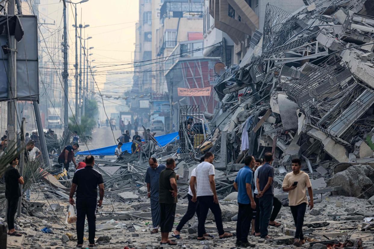 Residents walk along a debris-strewn street in front of a building that collapse during an Israeli air strike (MAHMUD HAMS/AFP via Getty Images)