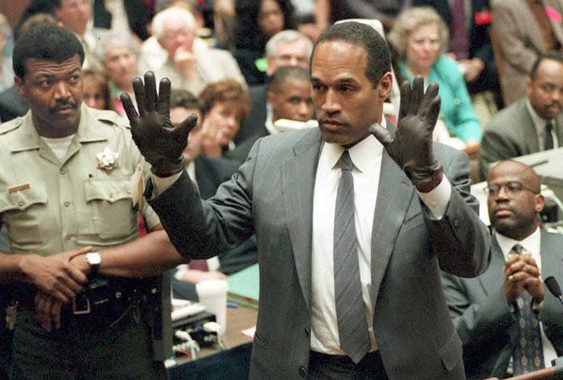 O.J. Simpson shows the jury a new pair of Aris extra-large gloves, similar to the gloves found at the Bundy and Rockingham crime scene 21 June during his double murder trial in Los Angeles. Depety Sheriff Roland Jex(L) and Prosector Christopher Darden(R) look on. - Photo: POO/AFP (Getty Images)