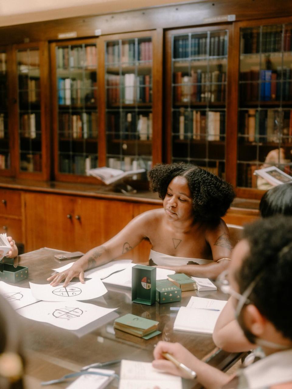 Star Feliz sits at a table surrounded by oracle deck imagery in the library of the Philosophical Research Society.