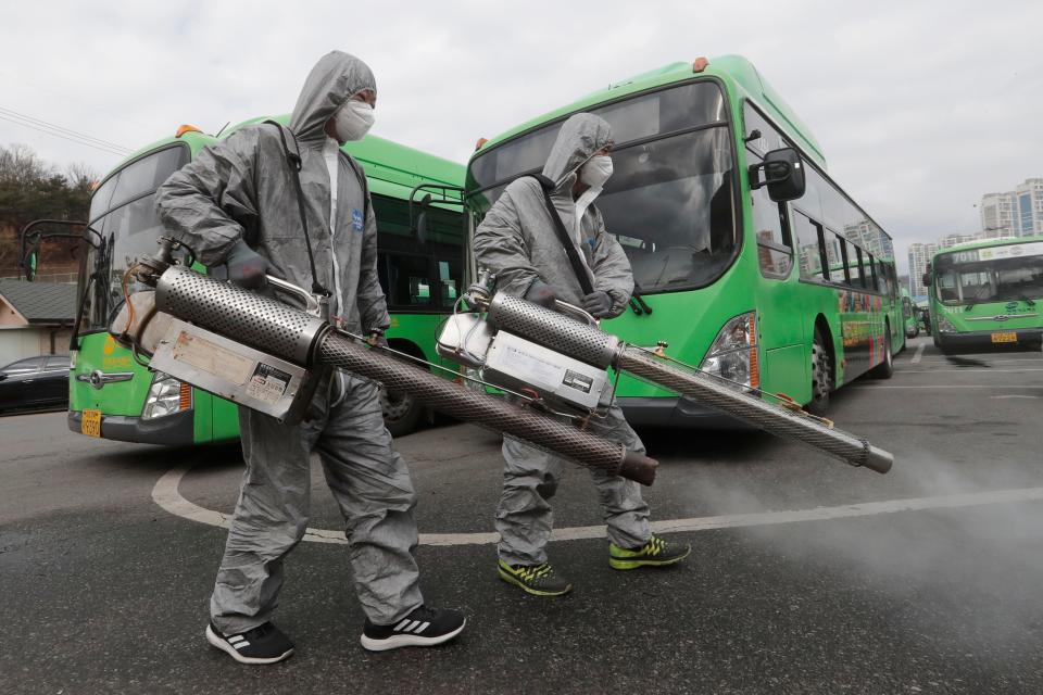 Workers wearing protective suits spray disinfectant as a precaution against the coronavirus at a bus garage in Seoul, South Korea, Feb. 26, 2020. The number of new virus infections in South Korea jumped again Wednesday and the U.S. military reported its first case among its soldiers based in the Asian country, with his case and many others connected to a southeastern city with an illness cluster.