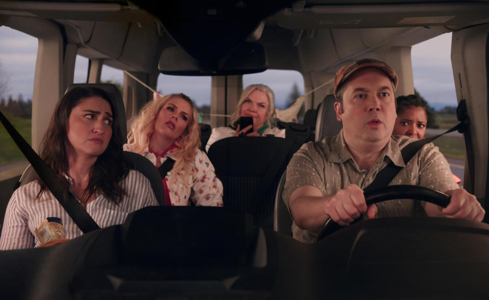 Interior shot of a minivan with a man driving nervously and four adult women as passengers; still from 'Girls5eva'