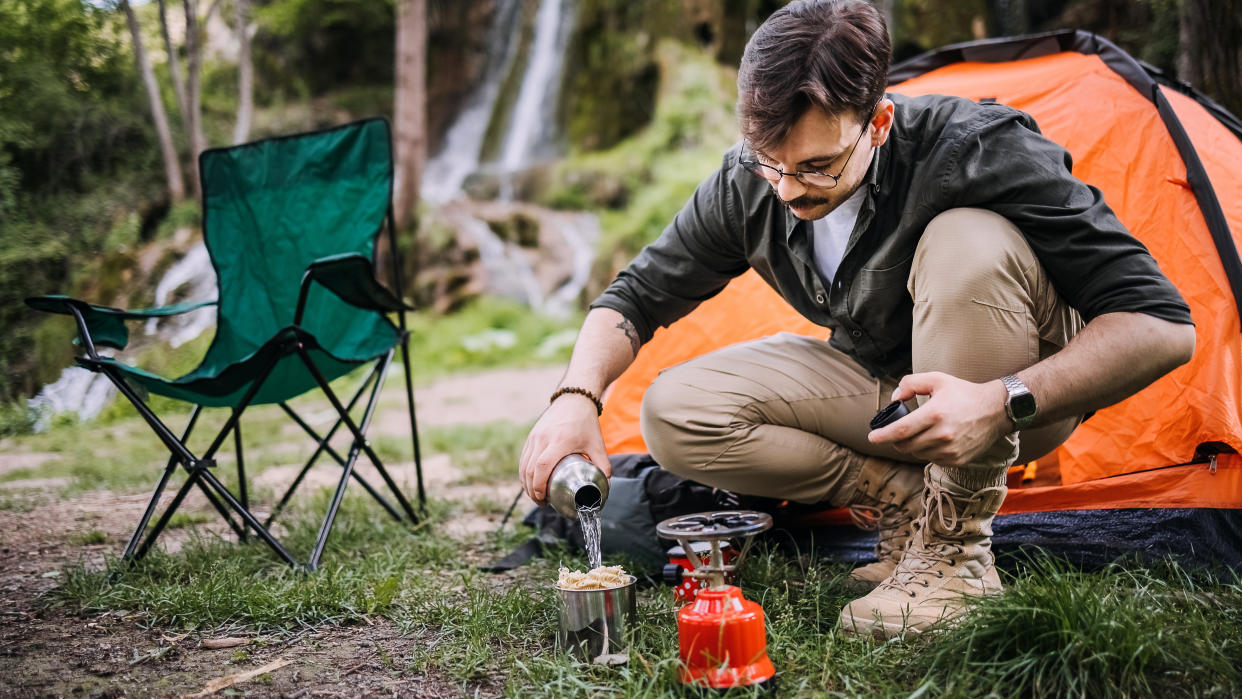  Man using camping stove to prepare pasta outside tent. 