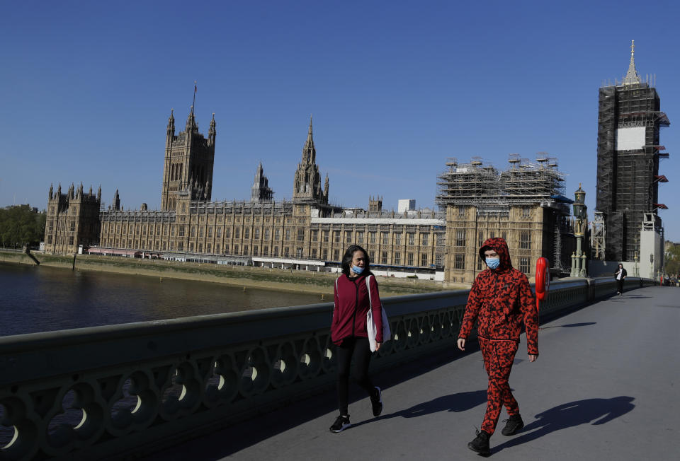 People wear masks as they walk near Britain's Houses of Parliament as the country is in lockdown to help curb the spread of coronavirus, in London, Tuesday, April 21, 2020.