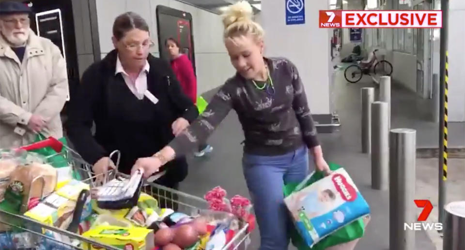 The alleged shoplifter grabs a few items while the Woolworths employee holds the trolley.