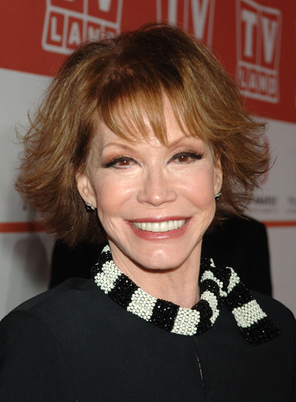 Woman smiling at event in black outfit with checkered neck detail