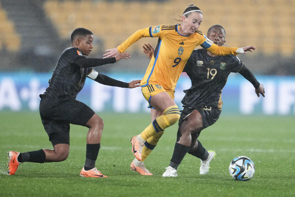 Sweden's Kosovare Asllani, centre, battles for the ball with South Africa's Lebohang Ramalepe, left, and Kholosa Biyana, right, during the Women's World Cup Group G soccer match between Sweden and South Africa in Wellington, New Zealand, Sunday, July 23, 2023. (AP Photo/John Cowpland )