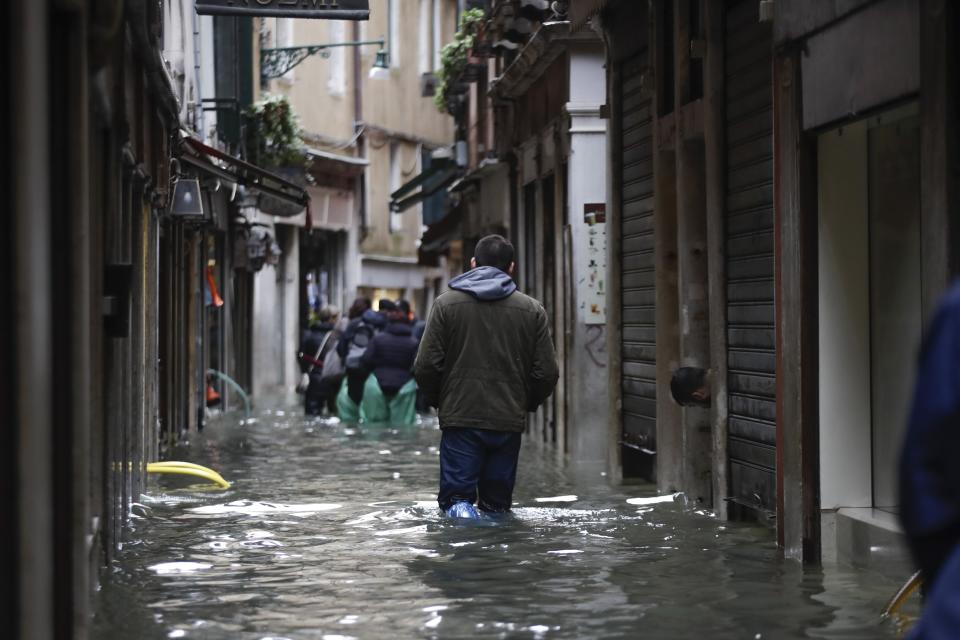 People wade their way through water in Venice, Italy, Friday, Nov. 15, 2019. Waters are rising in Venice where the tide is reaching exceptional levels just three days after the Italian lagoon city experienced its worst flooding in more than 50 years. (AP Photo/Luca Bruno)