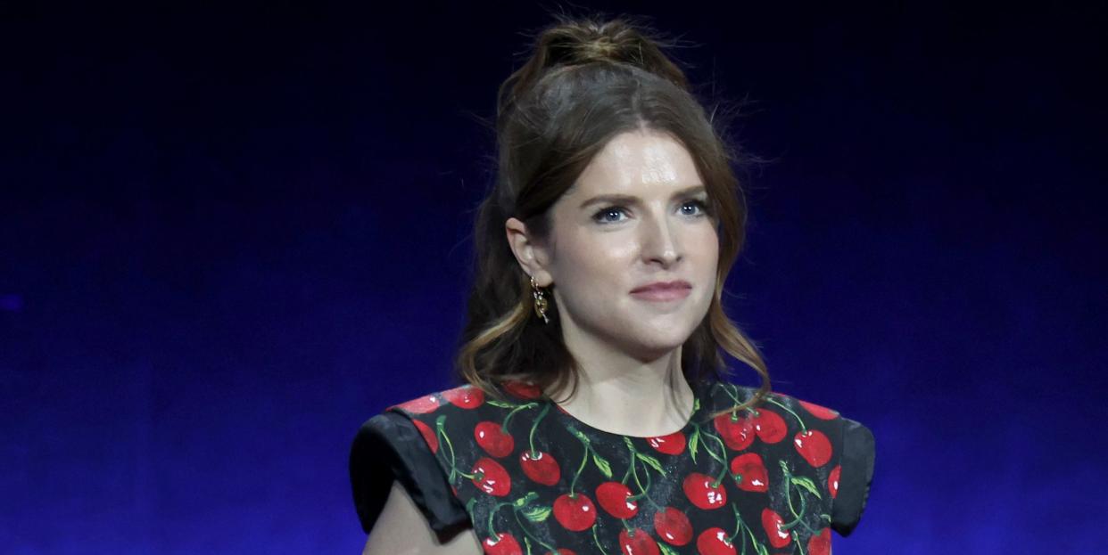 anna kendrick in a black dress with vine tomatoes, holding a microphone behind her back