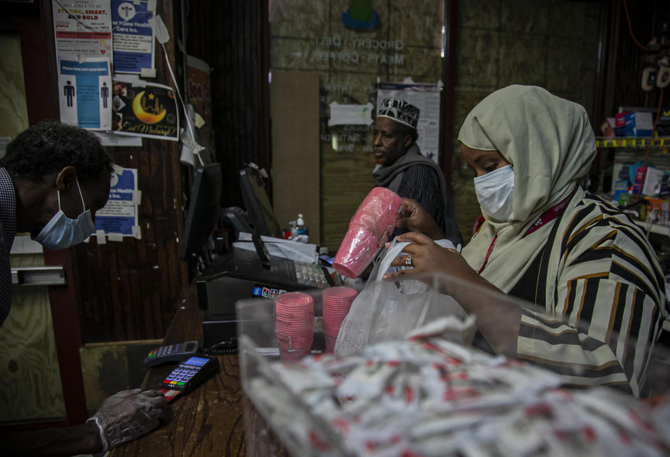 Hibaq Mohamed (extrema derecha) trabaja en la tienda de comestibles de productos somalíes de su abuelo en Minneapolis el 30 de mayo del 2020. El local tiene el frente cubierto de tablones por los desemanes que se vienen sucediendo desde la muerte de George Floyd. (AP Photo/Bebeto Matthews)