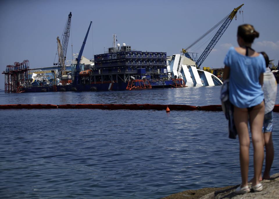 People look at the Costa Concordia cruise ship in the Tuscan Island of Isola del Giglio, Monday, July 15, 2013. Salvage crews are working against time to right and remove the shipwrecked Costa Concordia cruise ship, which is steadily compressing down on itself from sheer weight onto its granite seabed perch off the Tuscan island of Giglio. Salvage master Nick Sloane said Monday that the Concordia has compressed some 3 meters (10 feet) since it came to rest on the rocks Jan. 13, 2012 after ramming a jagged reef during a stunt ordered by the captain that cost the lives of 32 people. (AP Photo/Gregorio Borgia)