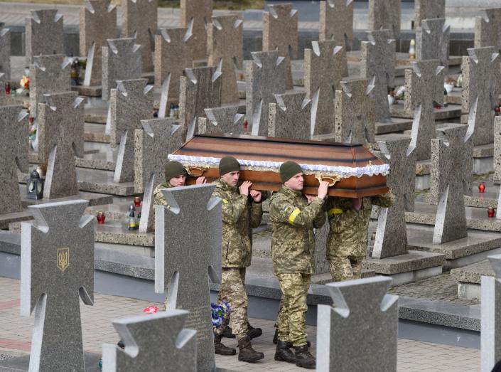 Servicemen carry a coffin in a cemetery.