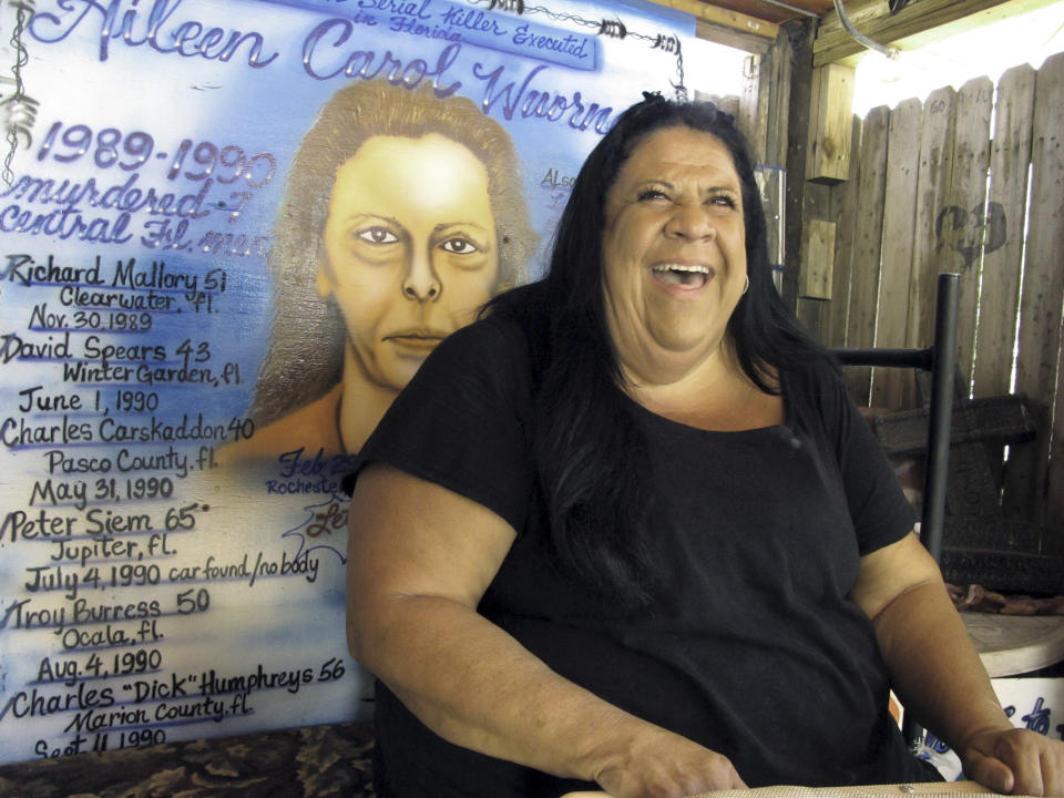 In this May 3, 2012 photo,airbush artist Ted E. Bear sits in front of a portrait she painted of serial killer Aileen Wuronos at The Last Resort Bar in Port Orange, Fla. Almost 22 years after Wuornos was arrested at The Last Resort, the curious still come to the place where she had her last drink. And at the Scoot Inn down the street, it's not unusual for people to walk into the motel office and ask to stay in the same room Wuornos did when she committed a string of murders that left seven men dead. (AP Photo/Brendan Farrington)