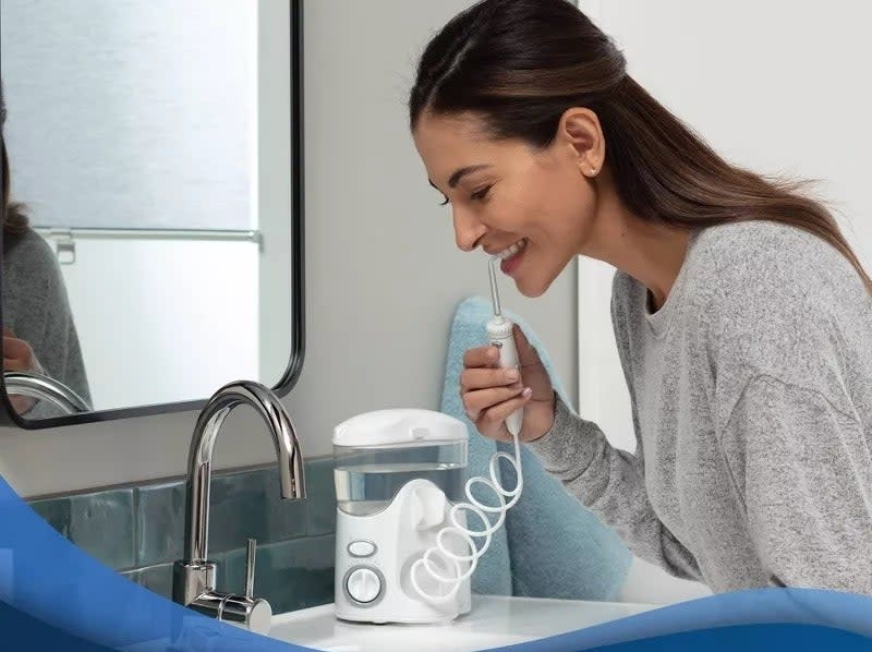 model uses a water flosser by the sink