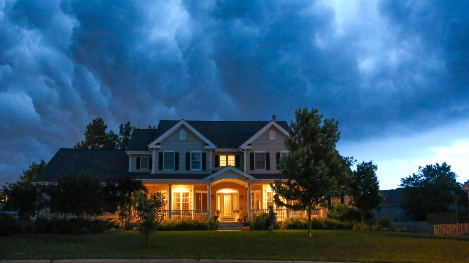 A well appointed house is lit up while a large thunderstorm moves in overhead.