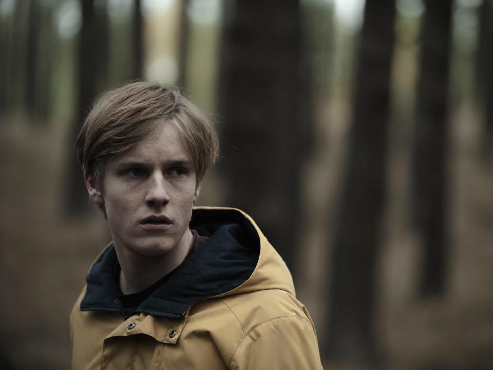 louis hofmann as jonas kahnwald in dark, a young man with blonde hair and a yellow rain coat