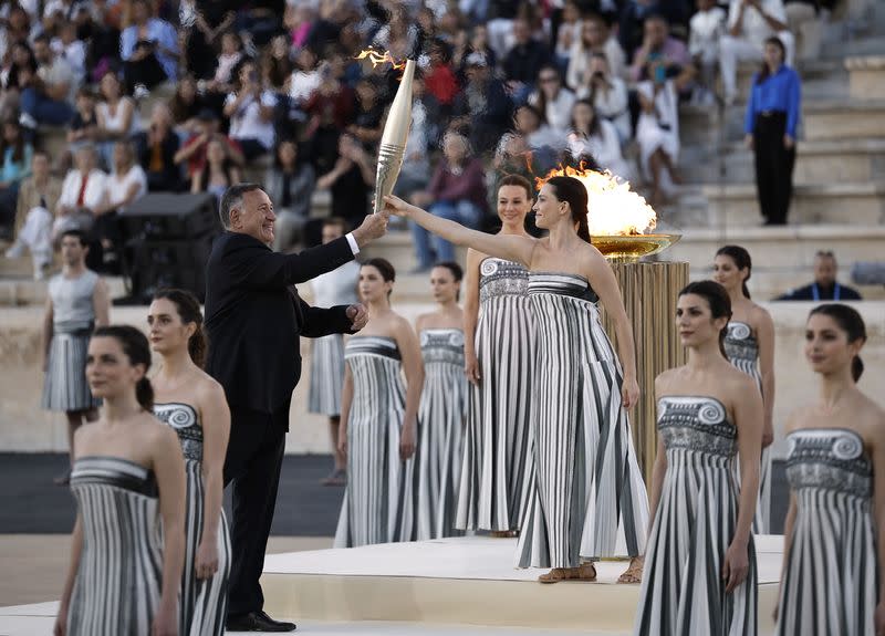 La actriz griega Mary Mina, que interpreta el papel de suma sacerdotisa, entrega la antorcha al presidente del Comité Olímpico Helénico y miembro del Comité Olímpico Internacional, Spyros Capralos, durante la ceremonia de entrega de la llama olímpica, en el estadio Panathinaiko de Atenas, Grecia