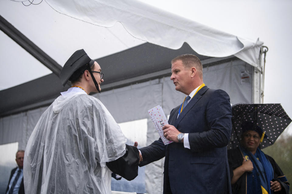 In this photo provided by University of Massachusetts Dartmouth, is billionaire Robert Hale, right, with a graduate student onstage at the graduation ceremony Thursday, May 16, 2024, in Dartmouth, Mass. Hale gifted graduates at the University of Massachusetts Dartmouth each with $1,000., with the condition that they give $500 away. Hale revealed the gift to more than 1,100 graduates. (Karl Christoff Dominey/University of Massachusetts Dartmouth via AP)