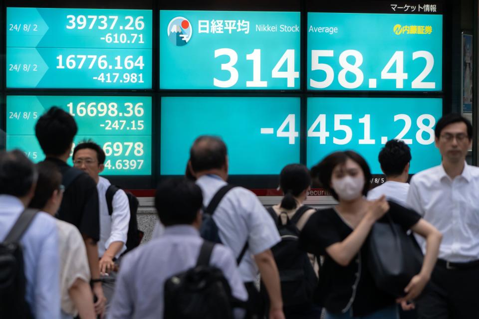 Pedestrians walk in front of monitors displaying the Nikkei 225 Stock Average figure outside a securities firm on Aug, 5, 2024 in Tokyo, Japan. The Nikkei 225 index in Tokyo experienced a significant decline, plunging nearly 7% on Aug. 4, 2024, as it fell to around 33,488.08 points shortly after the market opened. This drop, which came close to being a historic sell-off, is part of a broader global sell-off driven by concerns over the U.S. economy's stability amid high interest rates and disappointing hiring data, which has erased earlier gains that brought the Nikkei to all-time highs earlier this year.