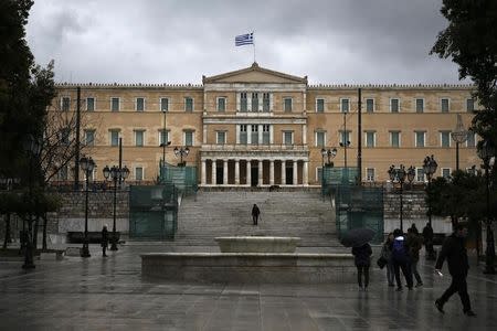 A Greek national flag flutters atop the parliament building as people make their way on Athens' Constitution Square (Syntagma), February 23, 2015. REUTERS/Alkis Konstantinidis