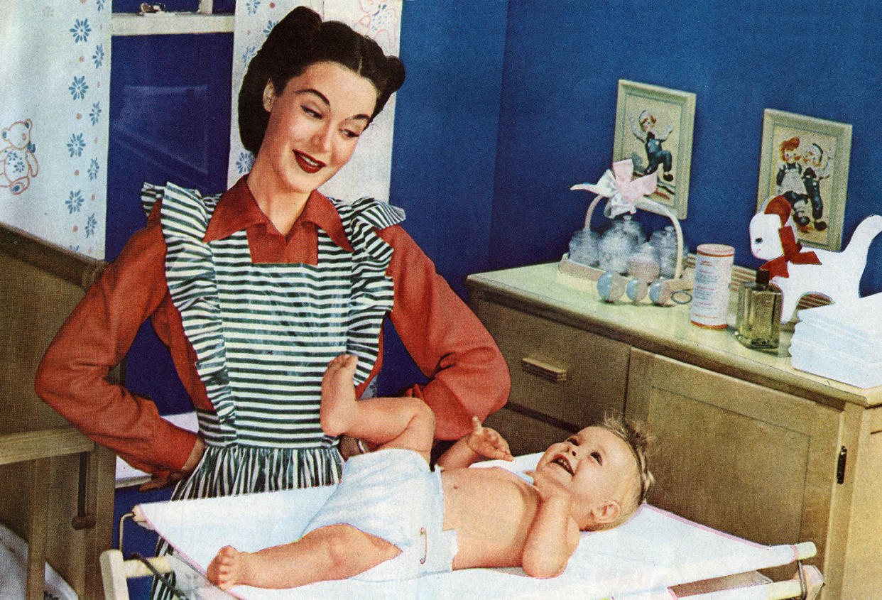 In this vintage screen print, a mother smiles as her happy baby lies on a changing table in a nursery. (Photo: GraphicaArtis/Getty Images)