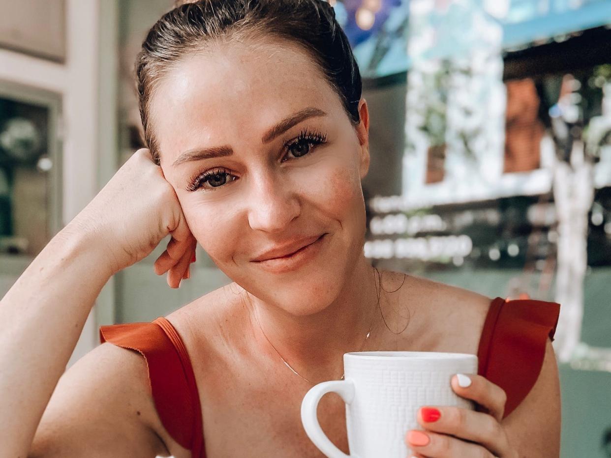 Lauren Burgess holding a mug on a table with an open book