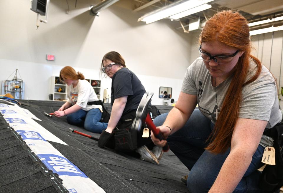 Quincy students Kelsie McFadden, Maddi Fifer, and Maicey McGinnis nail shingles to a floor level roof insides the Brach Area Carrer Center building trades classroom.