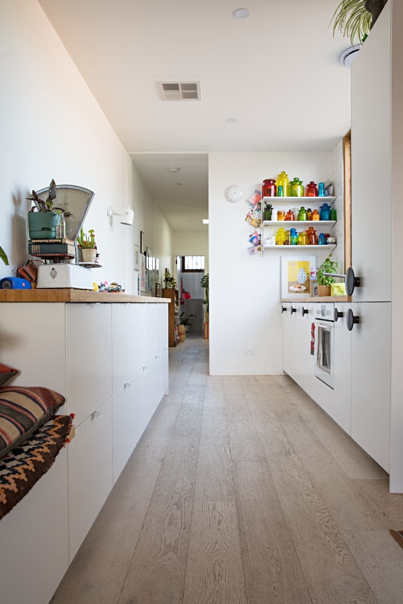 light wood flooring galley kitchen with white cabinets and white appliances