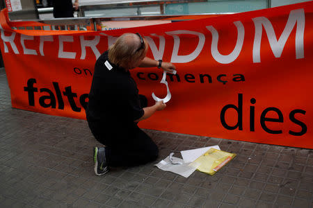 Catalan National Assembly (ANC) member and public worker of the Terrassa's town hall, Pep Rovira, places a sticker with the number five on a banner during a protest in favor of the banned October 1 independence referendum at Catalunya square in Barcelona, Spain, September 26, 2017. The banner reads, "Referendum. Where everything starts. 5 days left". REUTERS/Jon Nazca