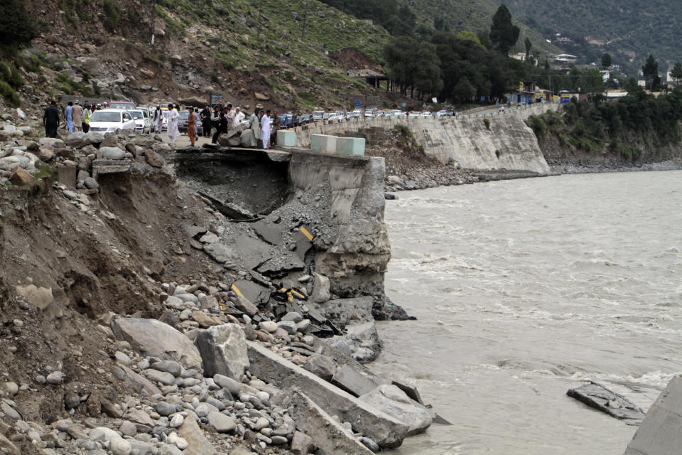 Passengers wait by a damaged road next to floodwaters, in Bahrain, Pakistan, Tuesday, Aug. 30, 2022. Disaster officials say nearly a half million people in Pakistan are crowded into camps after losing their homes in widespread flooding caused by unprecedented monsoon rains in recent weeks. (AP Photo/Naveed Ali)
