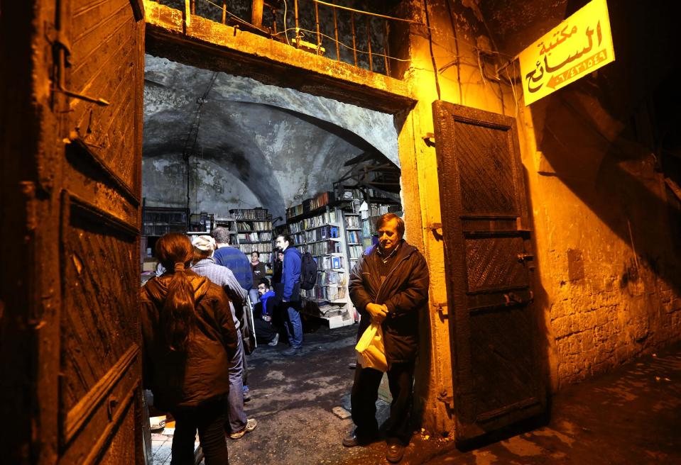 In this picture taken on Sunday, Jan. 5, 2014, Lebanese residents stand at the entrance of the Saeh (Tourist) Library which was set on fire by masked men, in the northern city of Tripoli, Lebanon. The Arabic placard on the top right, reads:"The Saeh Library". Books that were burnt in an arson attack targeting a crammed, chaotic and popular library in the northern Lebanese city of Tripoli have become the latest victim of the country's rising sectarian tensions.(AP Photo/Hussein Malla)