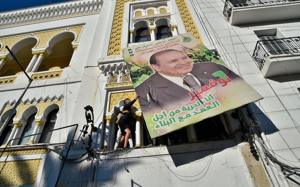 Algerian demonstrators tear down a large billboard with a picture of President Abdelaziz Bouteflika on it, during a demonstration against his candidacy for a fifth term, in Algiers, February 2019 - RYAD KRAMDI/AFP via Getty Images