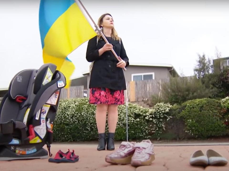 A protester with a Ukrainian flag and shoes repressing those confirmed killed by Russia (CBS 8 San Diego)