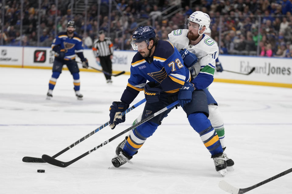 St. Louis Blues' Justin Faulk (72) and Vancouver Canucks' Filip Hronek battle for a loose puck during the second period of an NHL hockey game Tuesday, March 28, 2023, in St. Louis. (AP Photo/Jeff Roberson)
