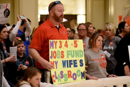 A supporter holds a sign that reads "My 3rd, 4th, and 5th jobs fund my wife's classroom" inside the state Capitol on the second day of a teacher walkout to demand higher pay and more funding for education in Oklahoma City, Oklahoma, U.S., April 3, 2018. REUTERS/Nick Oxford