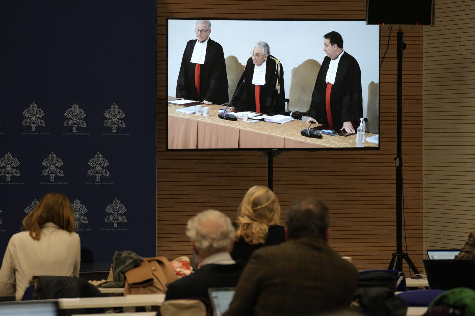 FILE - Reporters watch a screen showing Vatican tribunal president Giuseppe Pignatone reading the verdict of a trial against Cardinal Angelo Becciu and nine other defendants, in the Vatican press room, Saturday, Dec. 16, 2023. The Vatican's chief prosecutor has appealed a court verdict that, while finding a cardinal guilty of embezzlement, largely dismantled his theory of a grand conspiracy to defraud the Holy See of millions of euros. (AP Photo/Andrew Medichini, File)