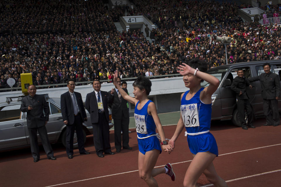 North Korean twin sisters Kim Hye Gyong (135) and Kim Hye Song (136) take a victory lap together inside Kim Il Sung Stadium after placing first and second respectively in the the women's Mangyongdae Prize International Marathon in Pyongyang, North Korea on Sunday, April 13, 2014. The annual race, which includes a full marathon, a half marathon, and a 10-kilometer run, was open to foreign tourists for the first time this year. (AP Photo/David Guttenfelder)