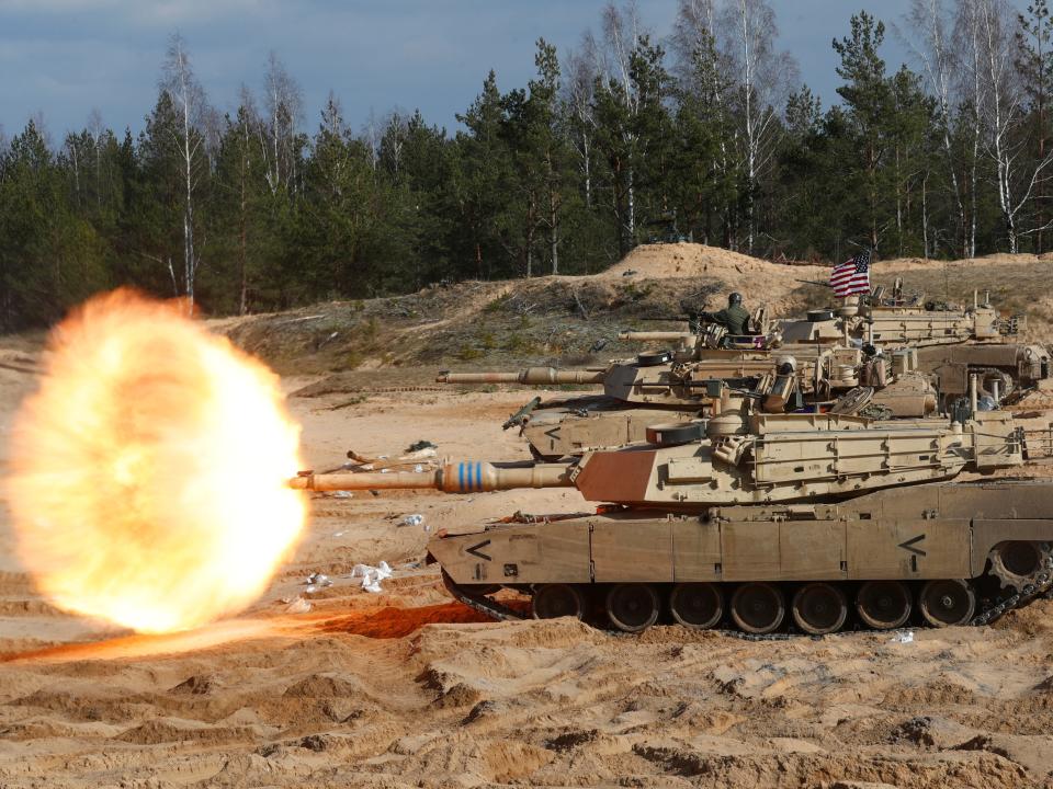 A M1A1 Abrams tank firing during NATO training exercise in an open field