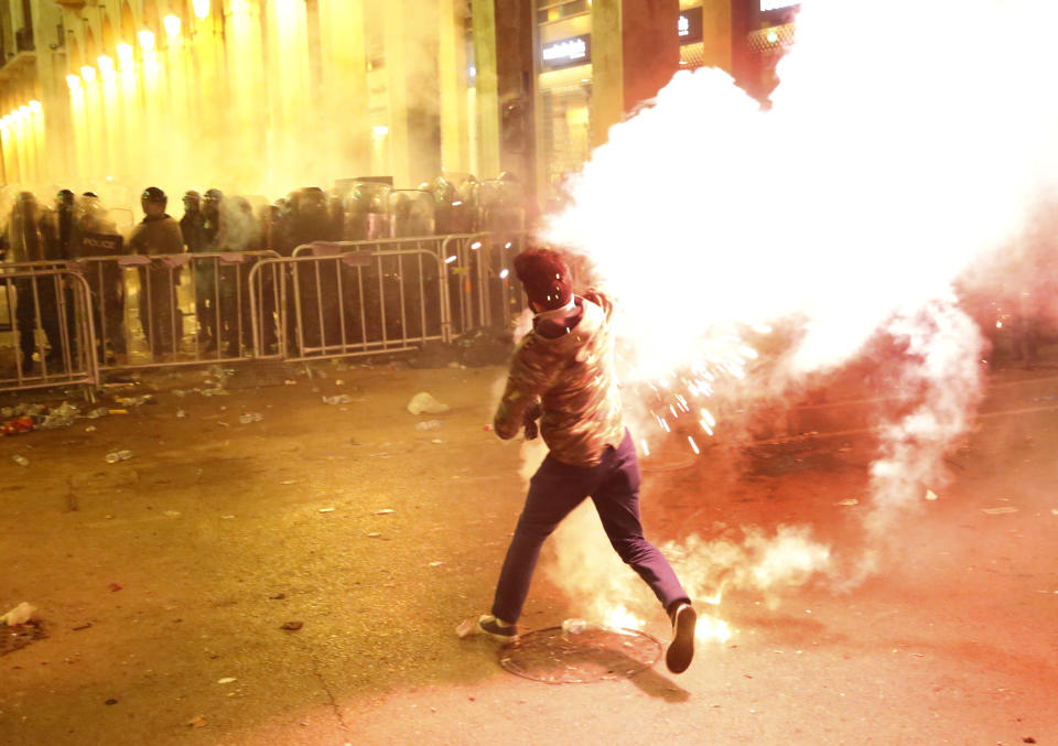 An anti-government protester throws flares against the riot police, background, during a protest near the parliament square, in downtown Beirut, Lebanon, Sunday, Dec. 15, 2019. Lebanese security forces fired tear gas, rubber bullets and water cannons Sunday to disperse hundreds of protesters for a second straight day, ending what started as a peaceful rally in defiance of the toughest crackdown on anti-government demonstrations in two months. (AP Photo/Hussein Malla)