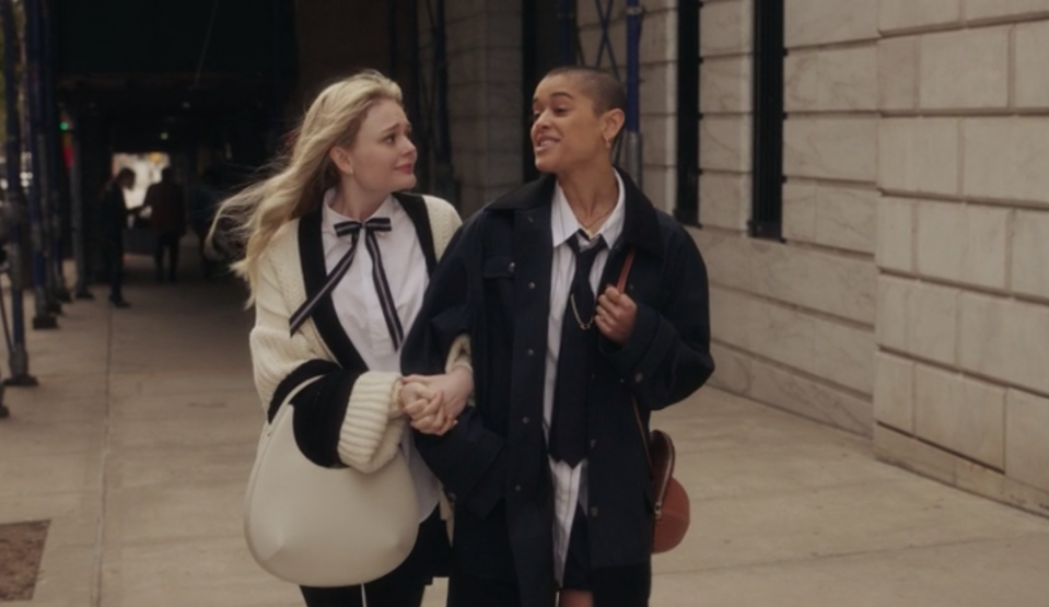 Audrey wears an oversize knit sweater with a skinny bow tie, and Julien wears a pin-striped button-up shirt, dark tie, and matching oversize jacket