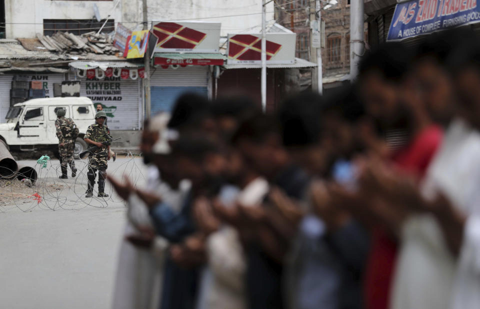 Indian paramilitary soldiers stand guard as Kashmiri Muslims offer Friday prayers on a street outside a local mosque during curfew like restrictions in Srinagar, India, Friday, Aug. 16, 2019. India's government assured the Supreme Court on Friday that the situation in disputed Kashmir is being reviewed daily and unprecedented security restrictions will be removed over the next few days, an attorney said after the court heard challenges to India's moves. (AP Photo/Mukhtar Khan)
