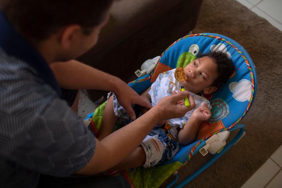 Man spoon feeds his toddler child, lying in a baby seat