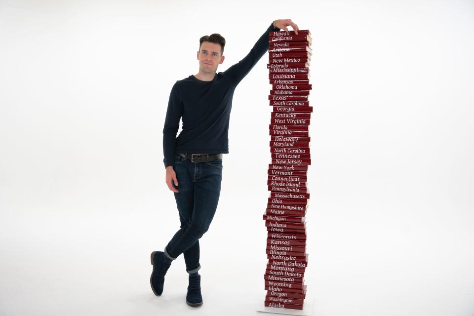 A promotional image of Mason Engel standing with a stack of books, each labeled with the name of one of the 50 states.