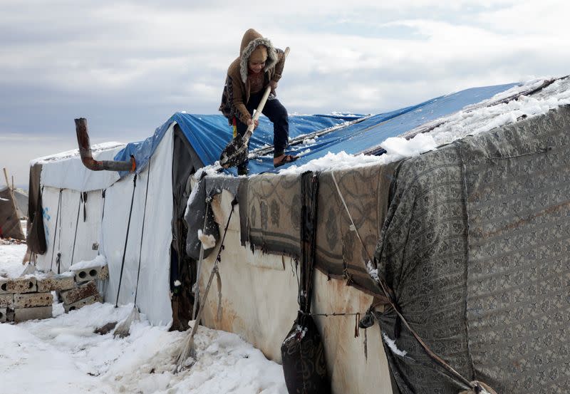 A girl removes snow from the top of a tent at a camp for internally displaced people, in northern Aleppo countryside