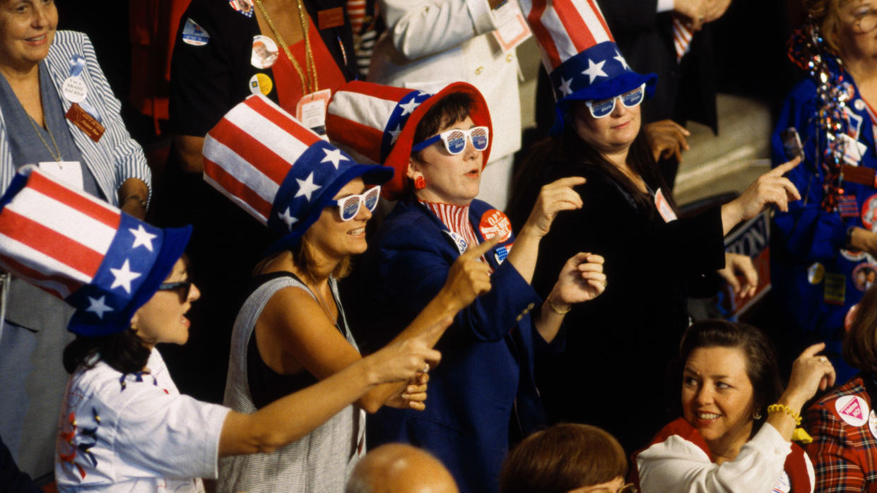 Democrats at a National Convention dance the Macarena in matching patriotic hats and sunglasses.