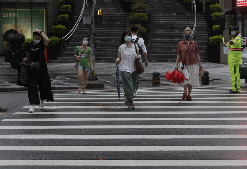 People wear face masks to protect against the spread of the coronavirus and walk in the light rain from approaching Typhoon In-Fa in Taipei, Taiwan, Thursday, July 22, 2021. (AP Photo/Chiang Ying-ying)